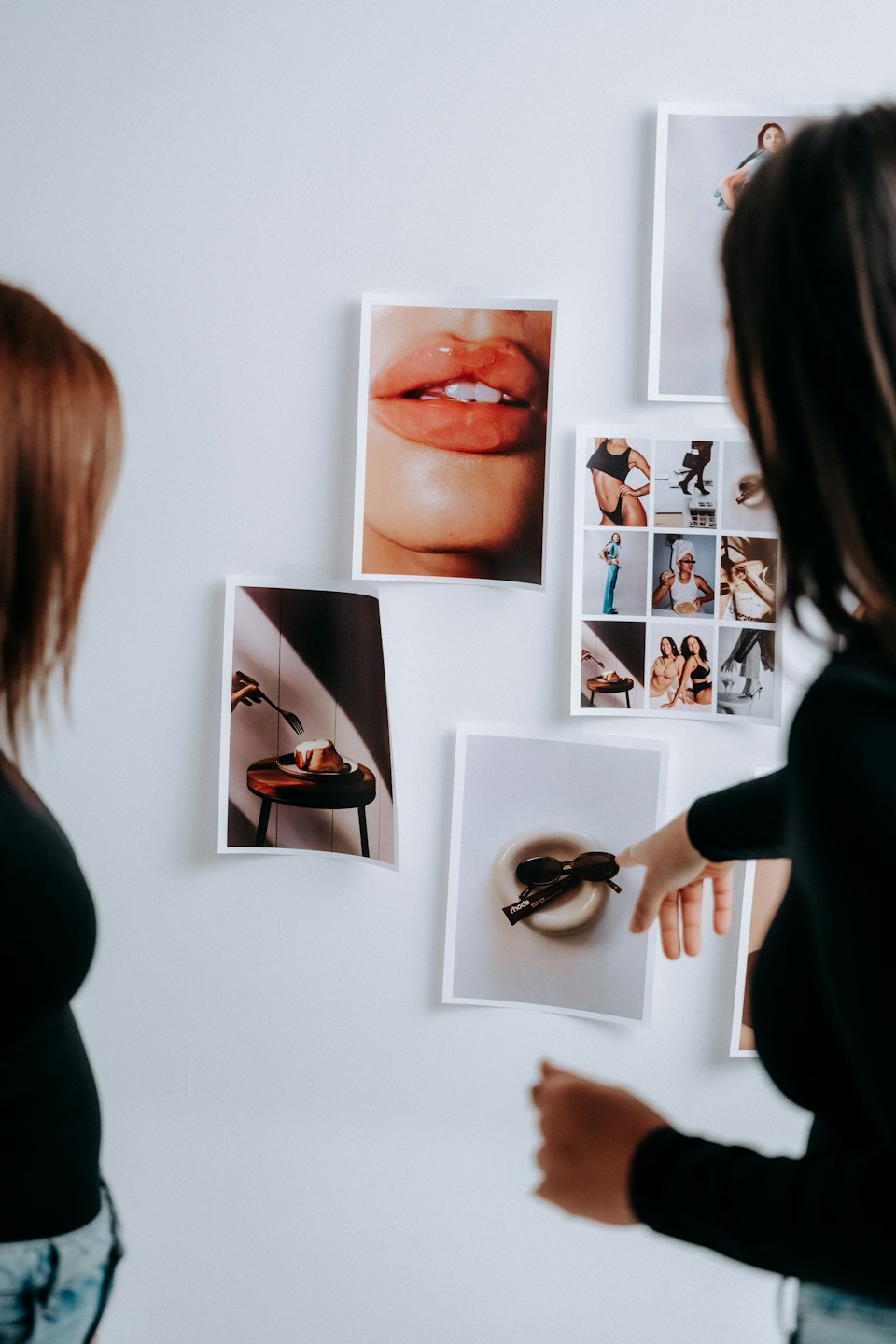 Twee mensen bekijken ingelijste foto's aan een witte muur.