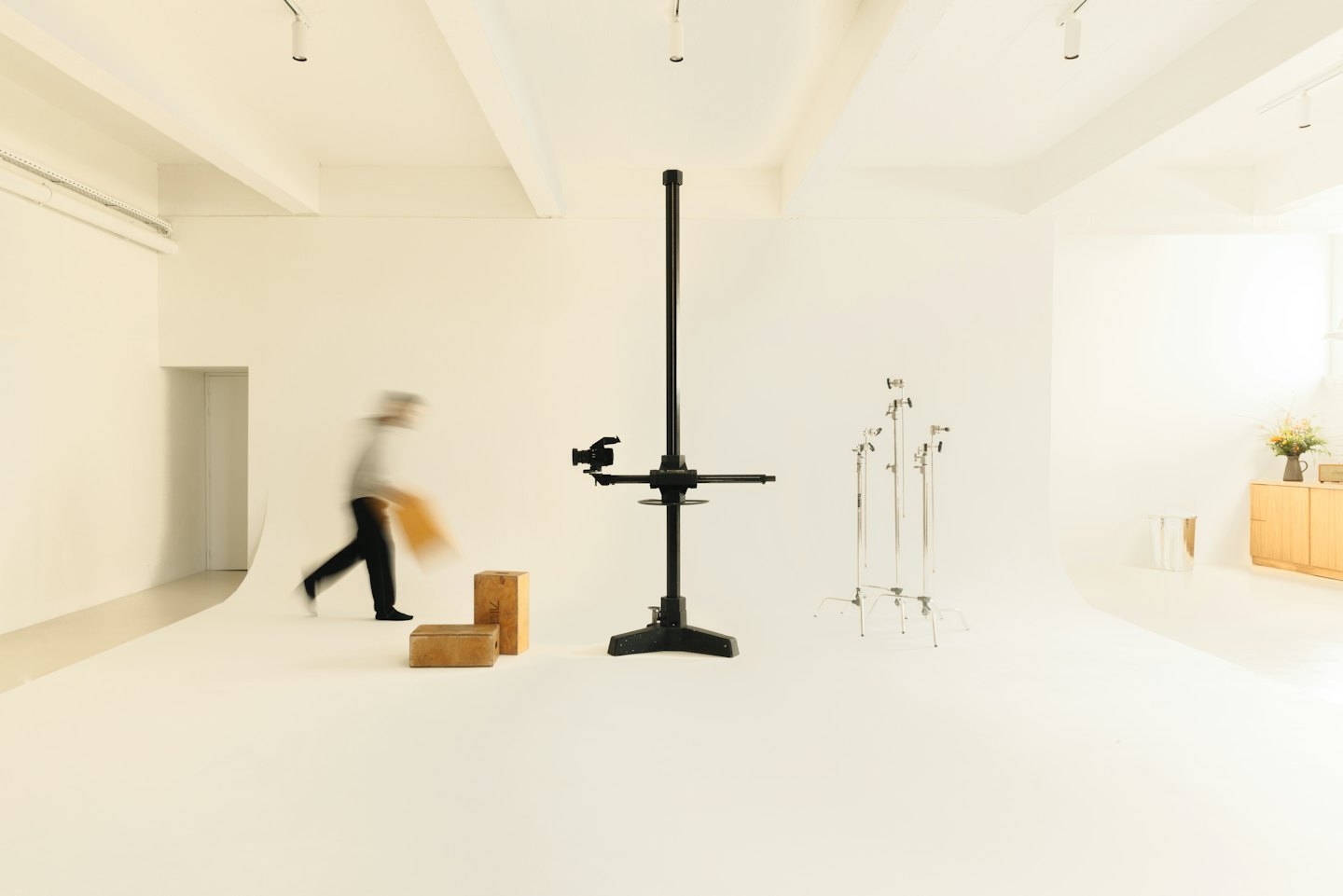 Persoon draagt rechthoekig object langs studioapparatuur.